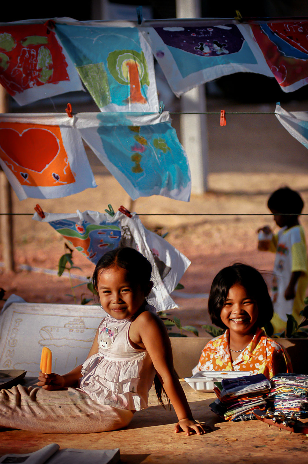 Thanawadee Ratana (9yrs right) with a friend, sitting beneath paintings done by members of the camp